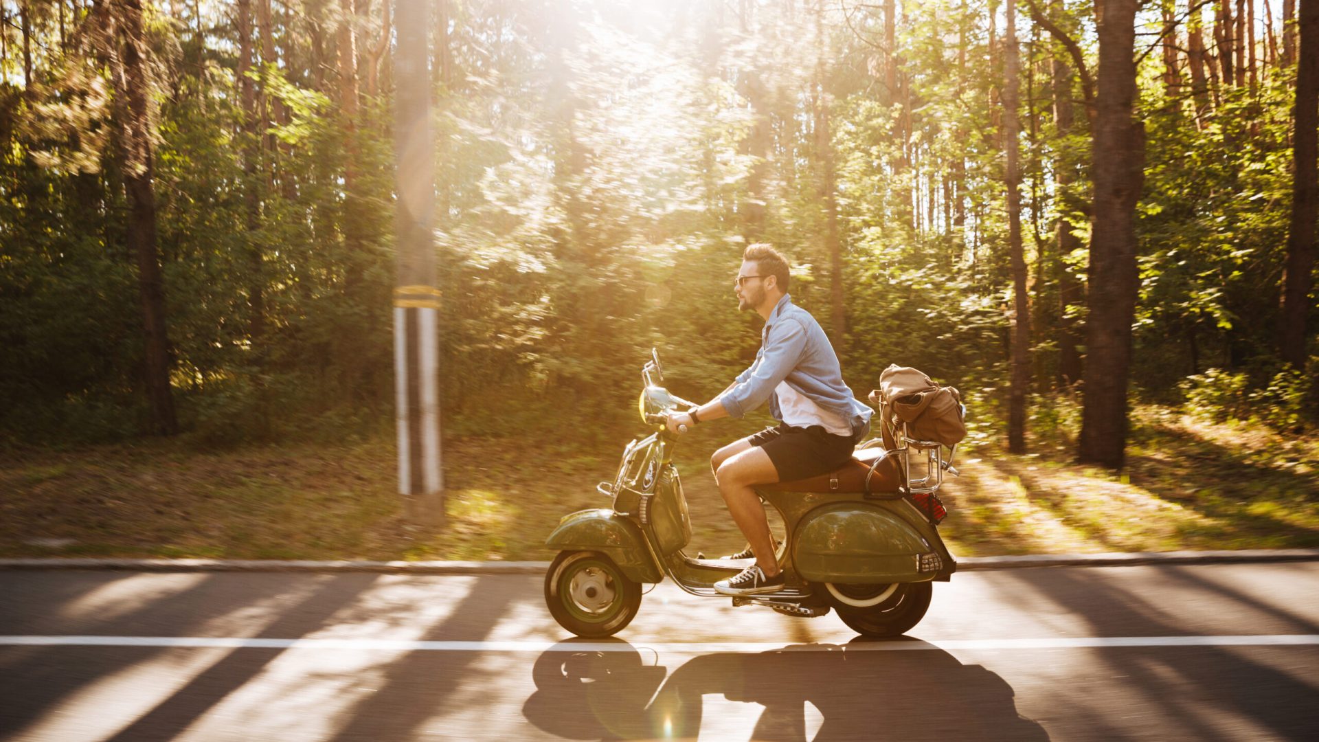 Picture of young bearded man on scooter outdoors. Looking aside.
