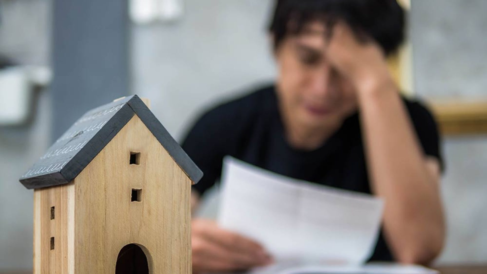 worried-man-holding-paper-with-model-house-table
